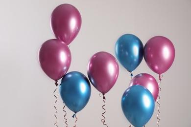 Photo of Bright balloons with ribbons flying on light background