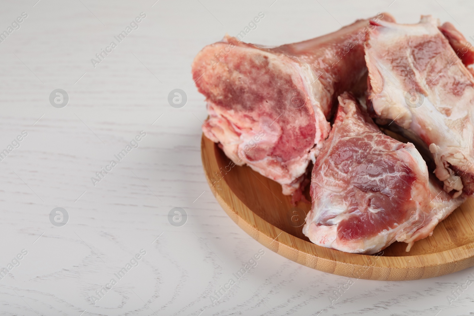 Photo of Plate with raw chopped meaty bones on white wooden table, closeup. Space for text