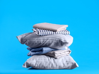Photo of Stack of clean bed sheets and pillows on blue background