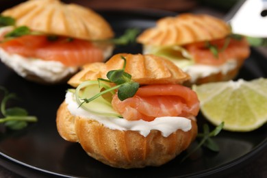 Photo of Delicious profiteroles with cream cheese, salmon and cucumber on plate, closeup
