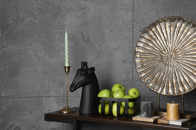 Photo of Wooden shelf with candles, decorative figure of giraffe, plate and apples against grey wall