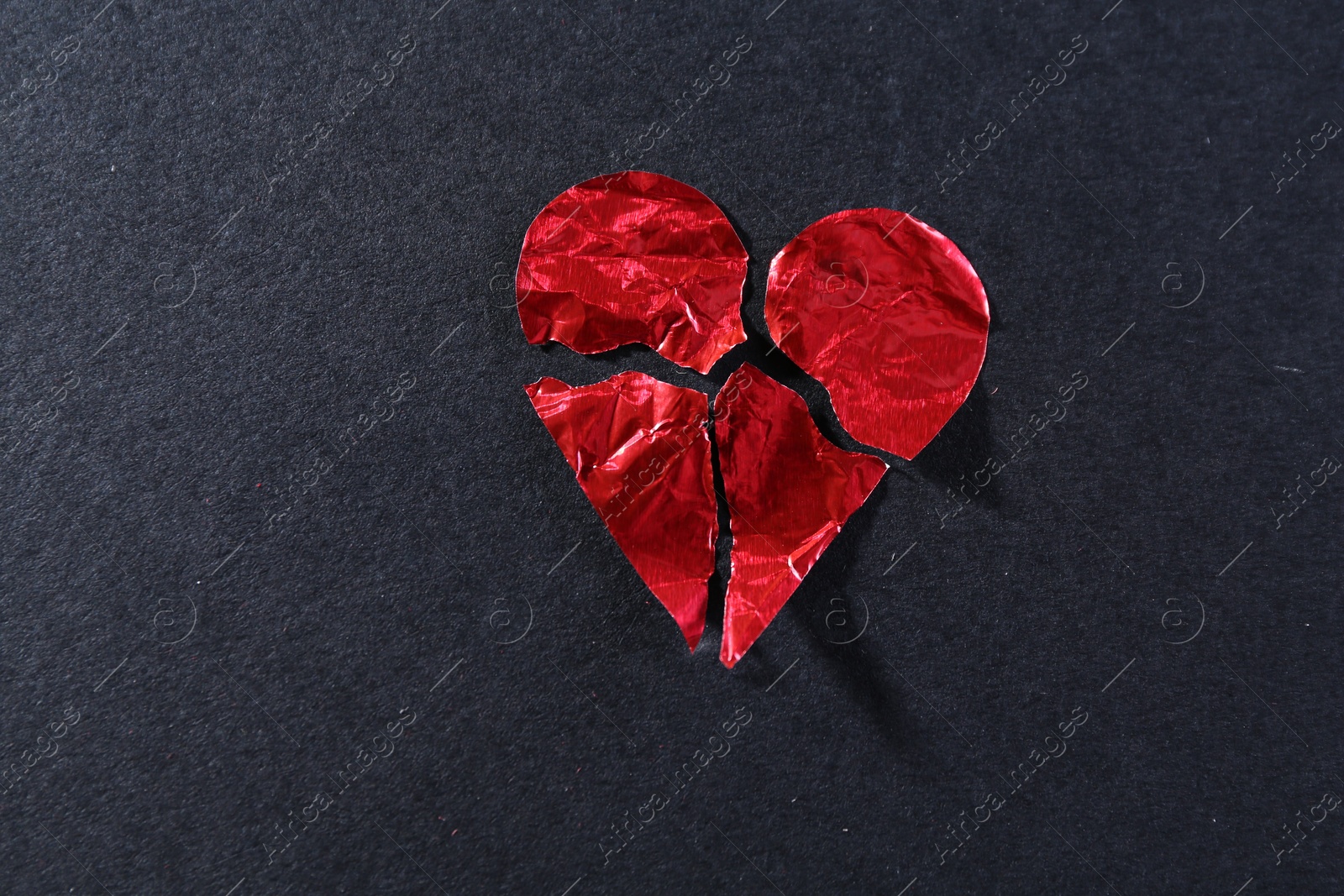 Photo of Red crumpled paper heart broken to pieces on black background, top view. Breakup concept