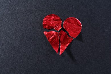 Photo of Red crumpled paper heart broken to pieces on black background, top view. Breakup concept