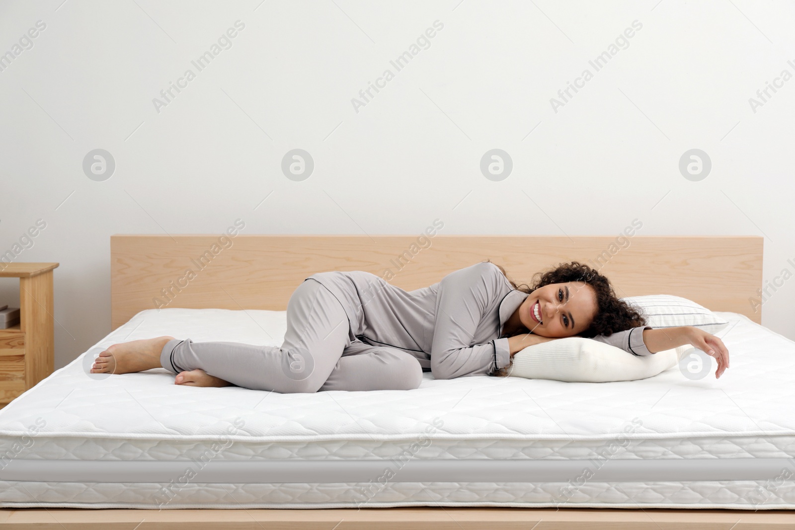 Photo of Happy young African American woman on bed with comfortable mattress and pillow at home