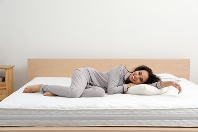 Happy young African American woman on bed with comfortable mattress and pillow at home