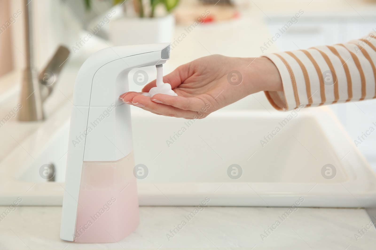 Photo of Woman using automatic soap dispenser in kitchen, closeup