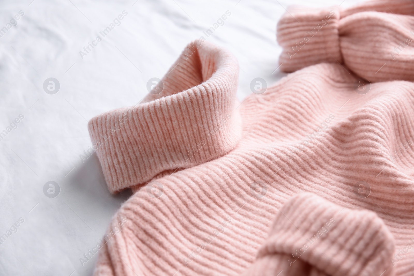 Photo of Pink warm sweater on white crumpled fabric, closeup