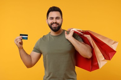 Smiling man with many paper shopping bags and credit card on orange background