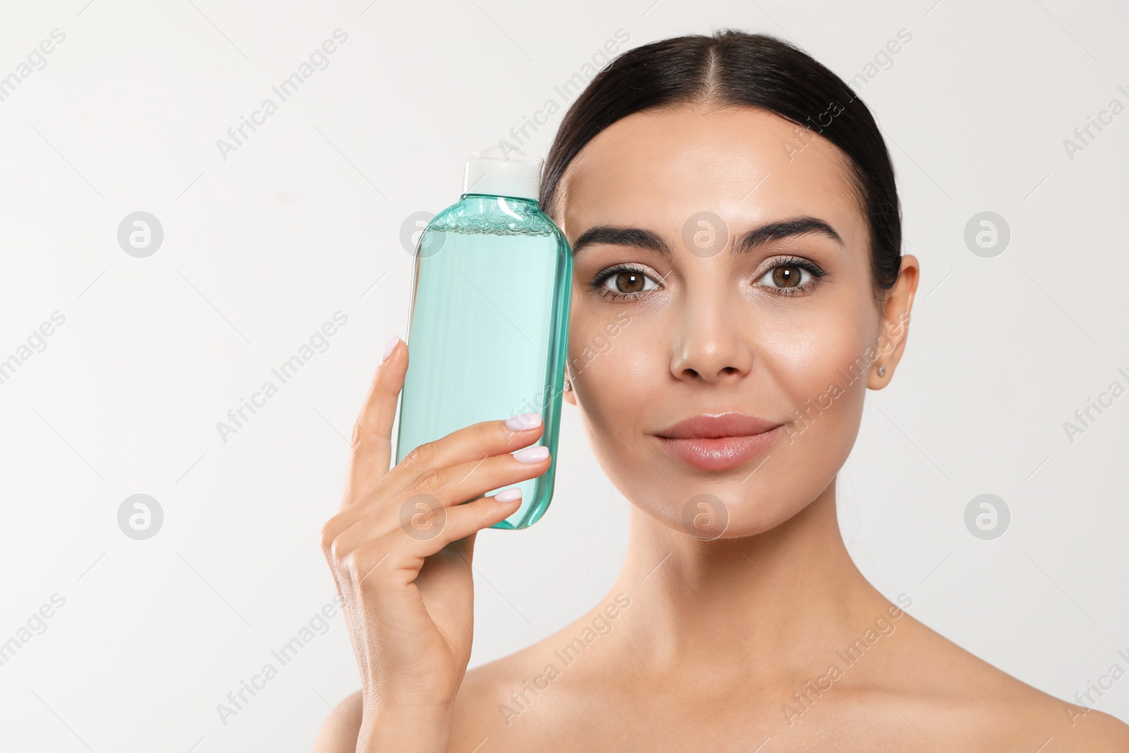 Photo of Young woman with micellar water on light grey background, space for text