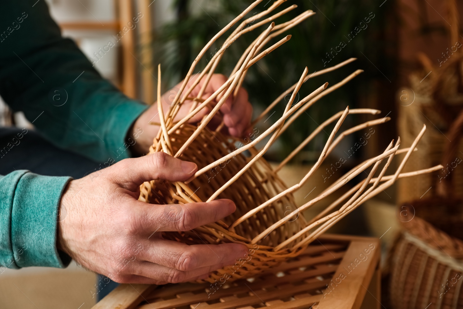 Photo of Man weaving wicker basket indoors, closeup view