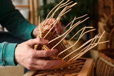 Photo of Man weaving wicker basket indoors, closeup view