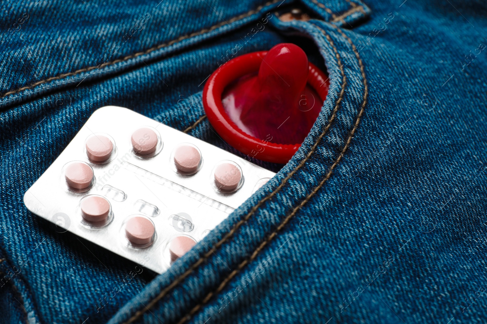 Photo of Red condom and birth control pills in pocket of jeans, closeup. Safe sex concept