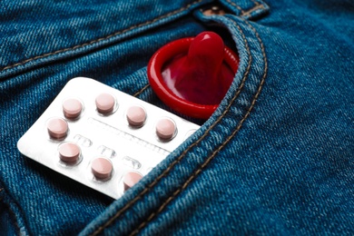 Red condom and birth control pills in pocket of jeans, closeup. Safe sex concept