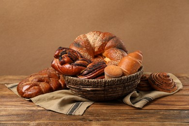 Photo of Wicker basket and different tasty freshly baked pastries on wooden table