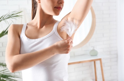 Woman touching armpit with feather indoors, closeup. Epilation procedure