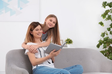 Happy mother and her teenage daughter with book at home