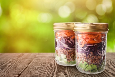 Image of Jars with healthy meal on wooden table against blurred background, space for text