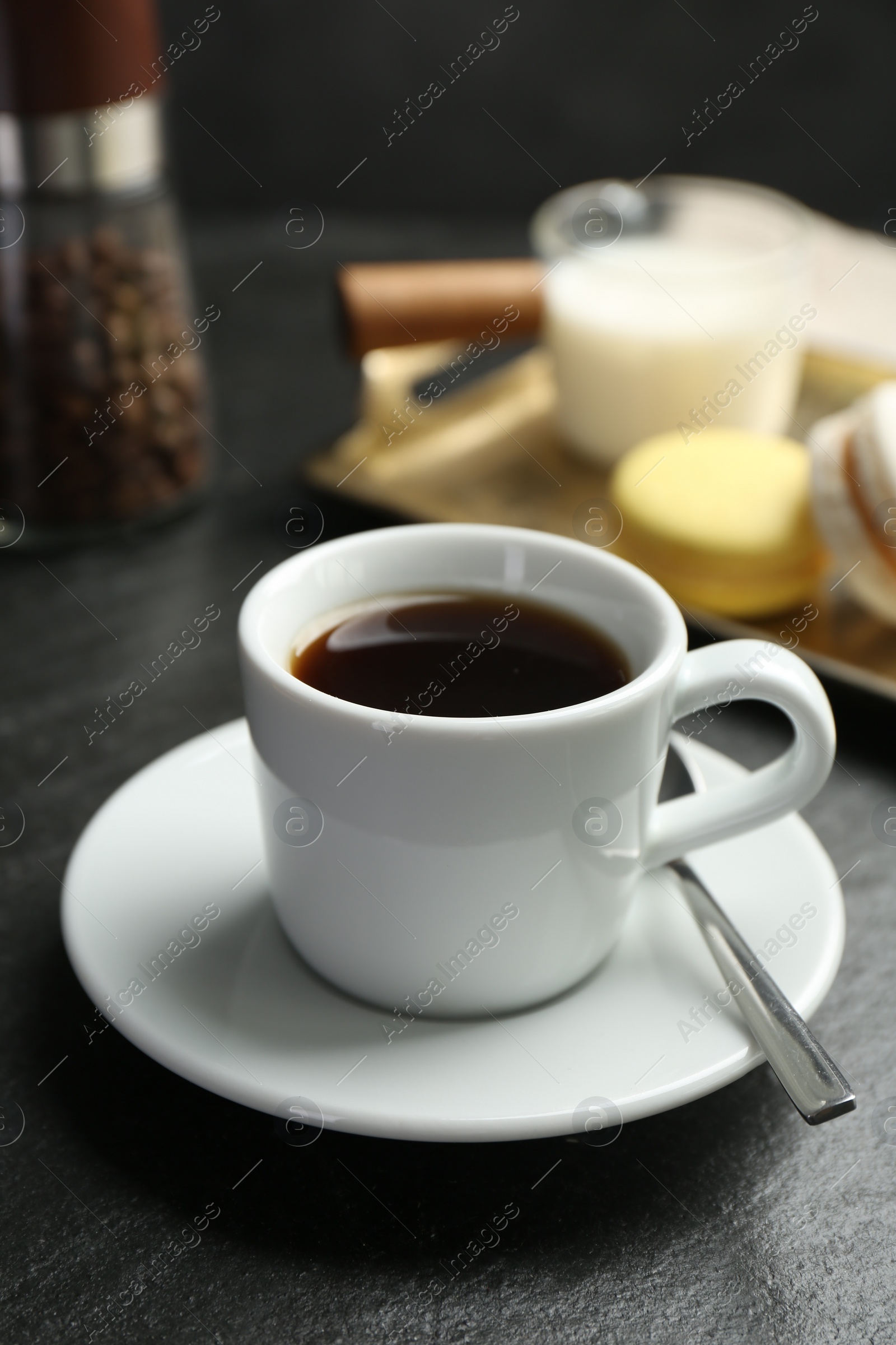 Photo of Hot coffee in cup, saucer and spoon on dark textured table, closeup