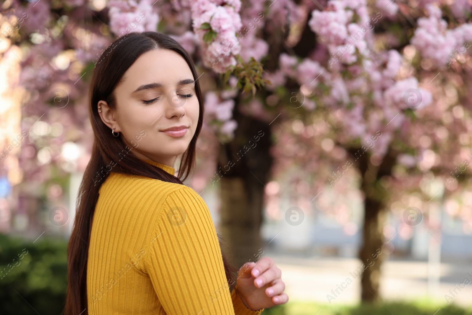 Photo of Beautiful woman near blossoming tree on spring day, space for text