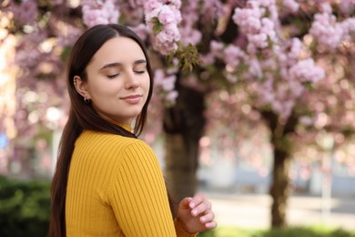 Photo of Beautiful woman near blossoming tree on spring day, space for text