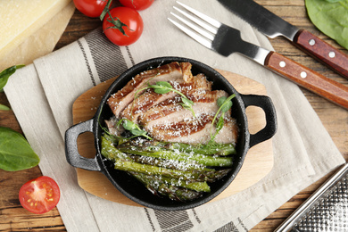 Photo of Tasty meat served with asparagus and sprouts in portioned frying pan on table, flat lay