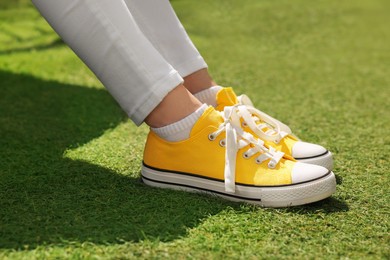 Woman in yellow classic old school sneakers on green grass outdoors, closeup
