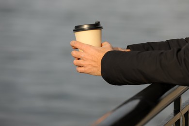 Man holding paper coffee cup outdoors, closeup