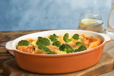 Tasty broccoli casserole in baking dish on wooden board