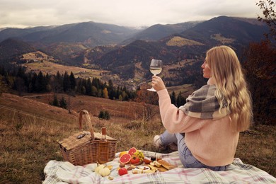 Image of Young woman with glass of wine having picnic in mountains on autumn day