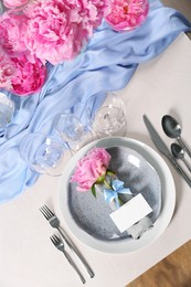 Stylish table setting with beautiful peonies, napkin and blank card, above view