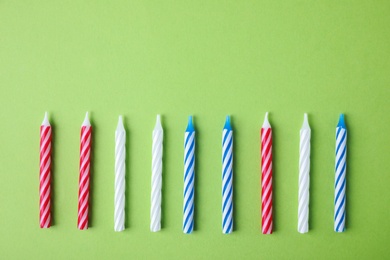 Colorful striped birthday candles on green background, flat lay