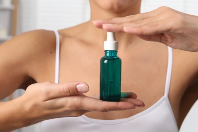 Woman with bottle of cosmetic serum on blurred background, closeup