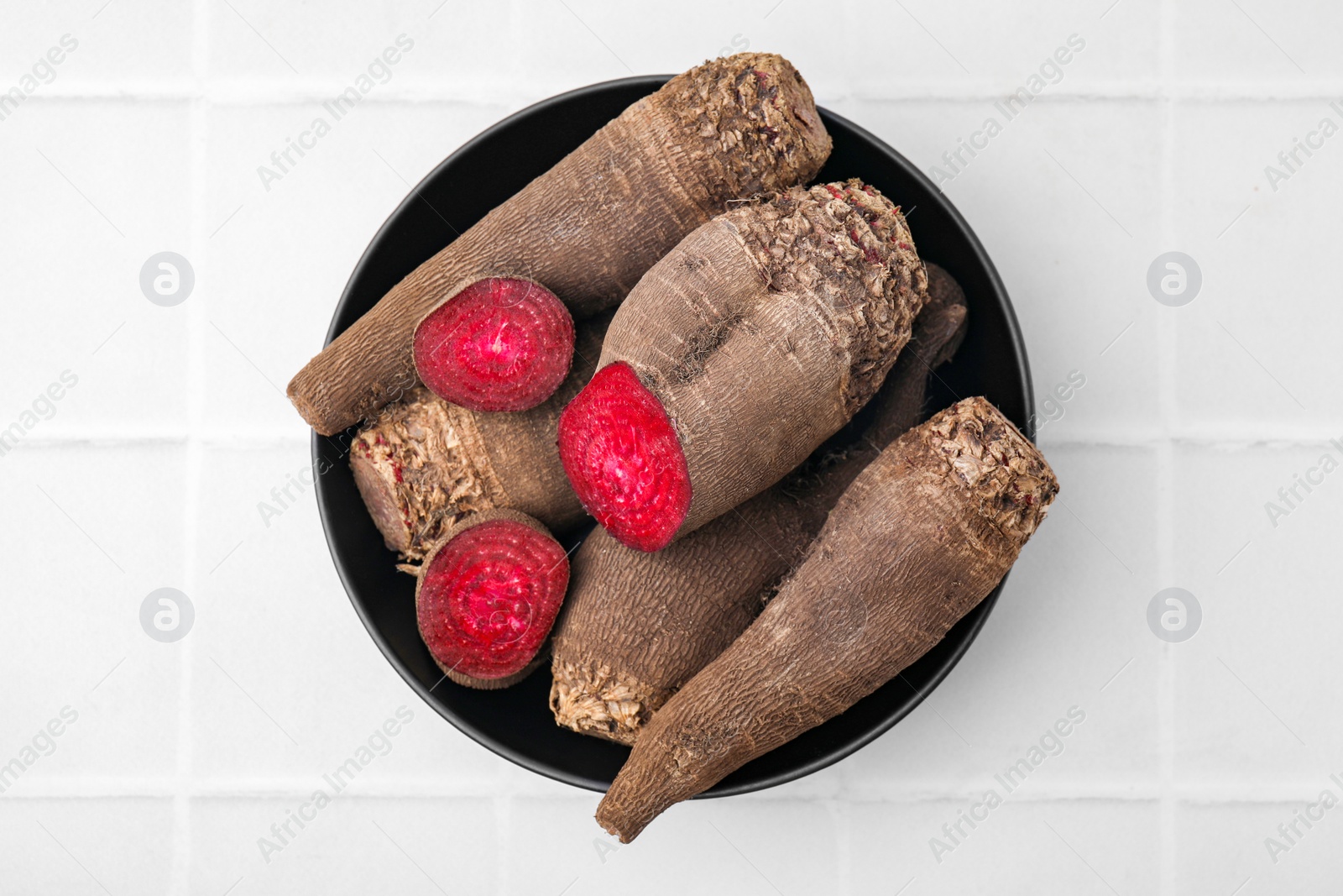 Photo of Whole and cut red beets in bowl on white table, top view