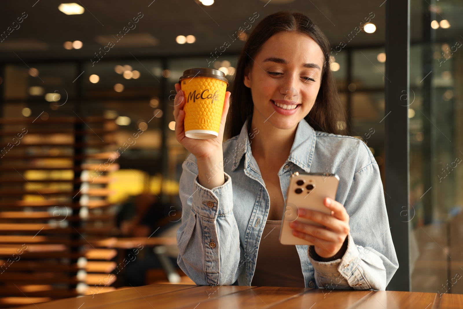 Photo of Lviv, Ukraine - September 26, 2023: Woman with hot McDonald's drink and smartphone in cafe
