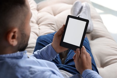 Man using e-book reader on sofa indoors, closeup