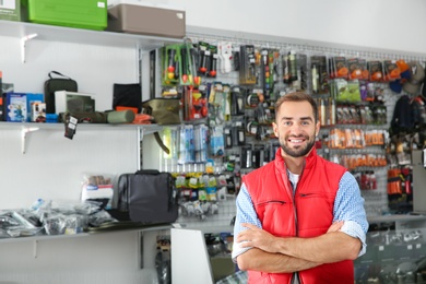 Salesman standing near showcase with fishing equipment in sports shop. Space for text