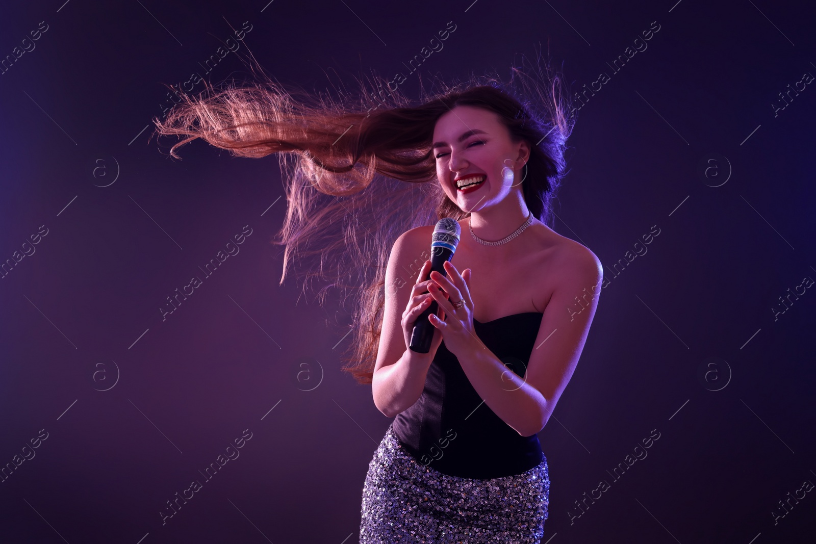 Photo of Emotional woman with microphone singing in neon lights on dark background