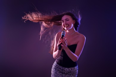 Photo of Emotional woman with microphone singing in neon lights on dark background