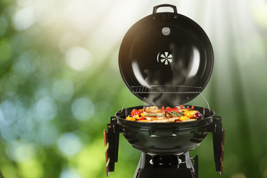 Image of Barbecue grill with meat products and vegetables outdoors on sunny day