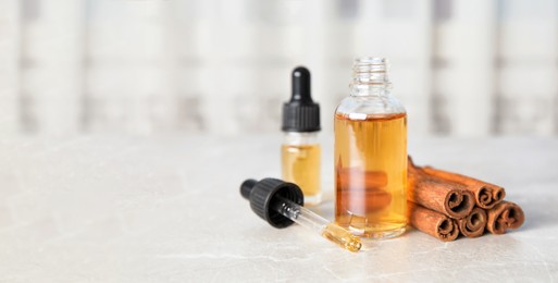 Image of Bottles of essential oils and cinnamon sticks on grey marble table, space for text. Banner design
