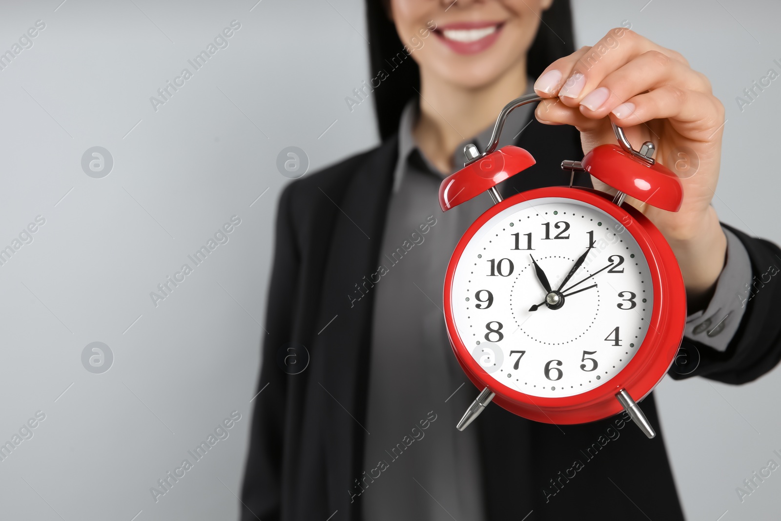 Photo of Businesswoman holding alarm clock on light grey background, closeup with space for text. Time management