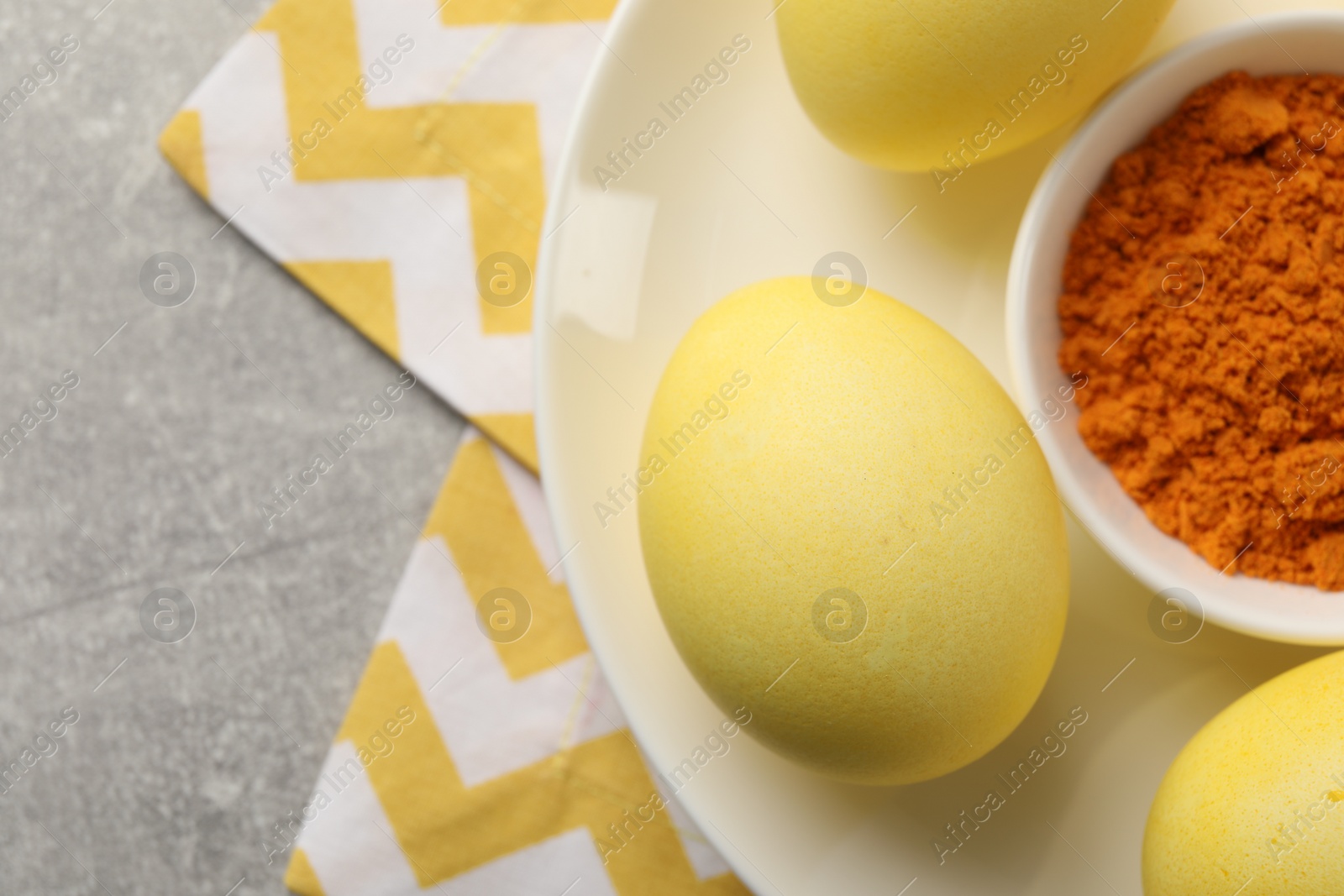 Photo of Yellow Easter eggs painted with natural dye and turmeric powder in bowl on light gray table, top view