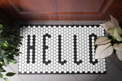 Photo of Stylish door mat with word HELLO and houseplants on floor, top view