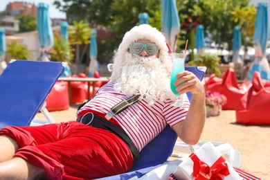 Photo of Authentic Santa Claus with cocktail resting on lounge chair at resort