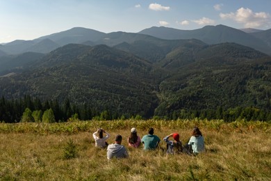 Image of Group of tourists sitting on hill in mountains, back view
