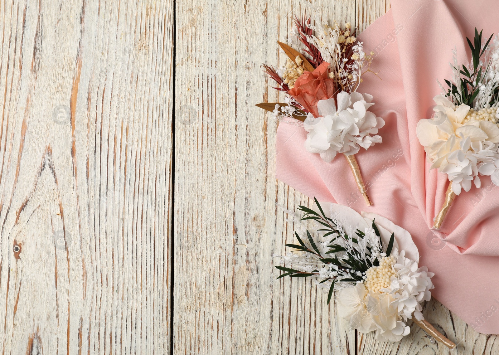 Photo of Stylish boutonnieres and pink fabric on light wooden table, top view. Space for text