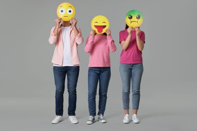 Photo of People covering faces with emoticons on grey background