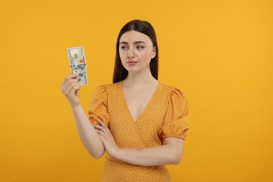 Sad woman with dollar banknote on orange background