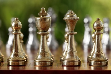 Photo of Golden chess pieces on game board against blurred background, closeup