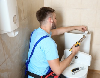 Photo of Professional plumber in uniform repairing toilet tank indoors